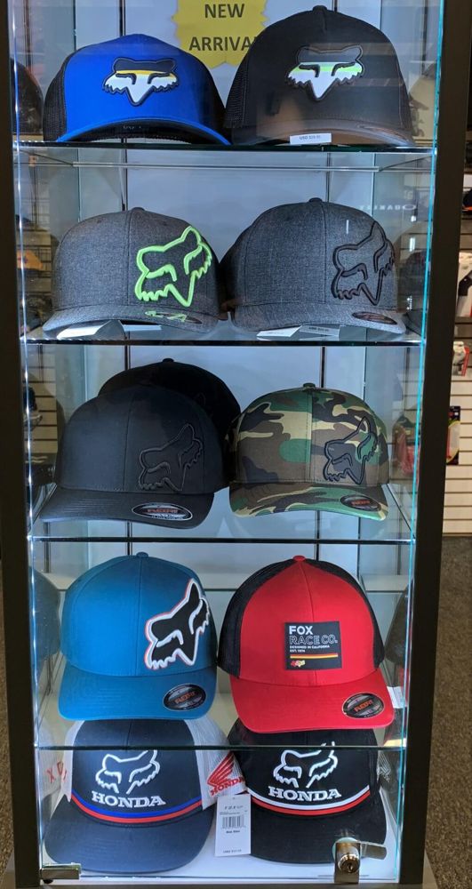 Lit glass display case of quality Fox brand hats. A few blue hats with white/gray Fox logos and a few gray hats with colored logos.