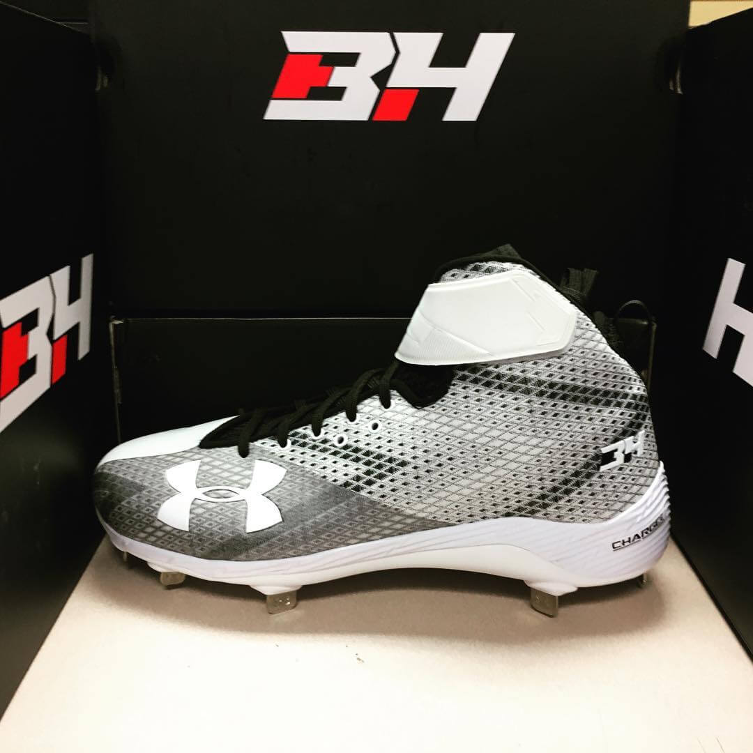 Under Armor brand white football cletes with metal spikes. Shoe is white with gray chevron pattern with repeating colors.