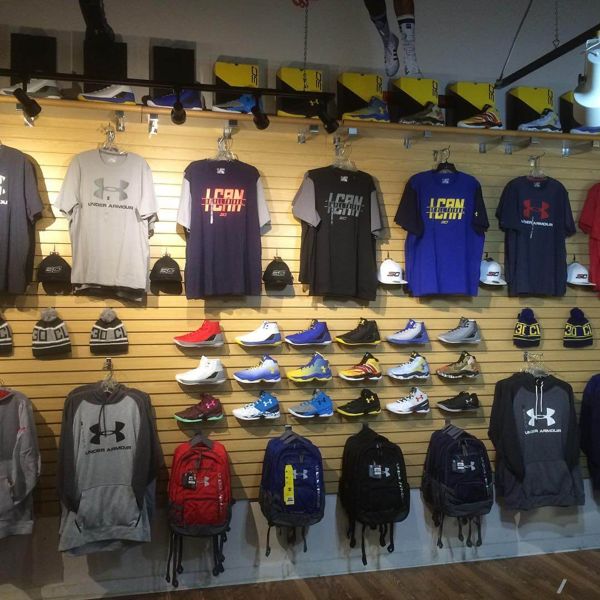 Retail wall display of various Under Armor apparel. Backpacks, shoes, shirts, and hoodies in various colors, styles, and sizes.